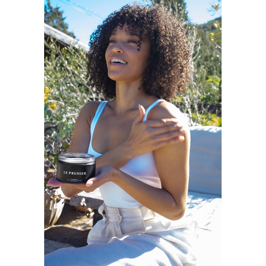 A woman holding a skincare product while enjoying the sunlight.