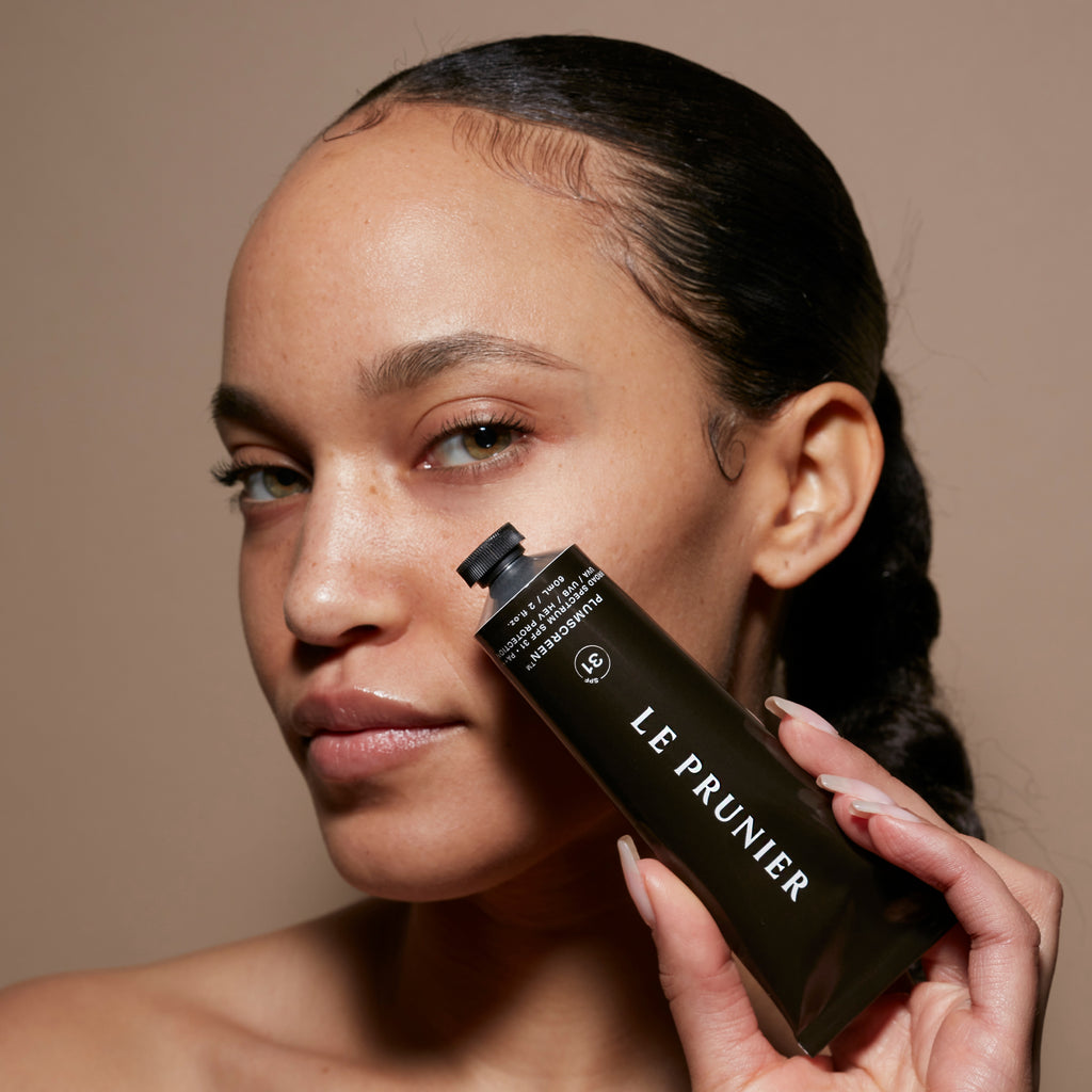 A woman showcasing a skincare bottle with the label "le prunier.