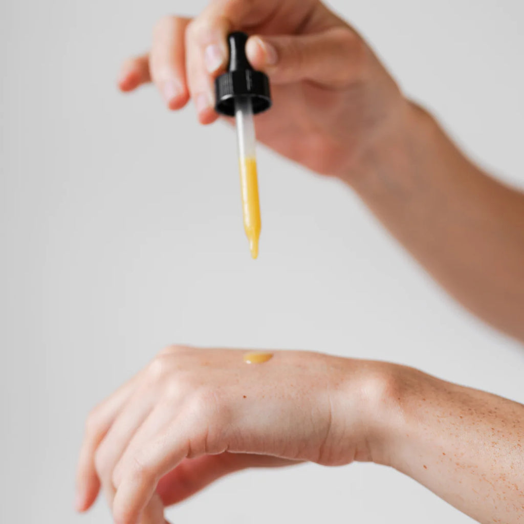 A person dispensing a viscous liquid from a dropper onto their arm.