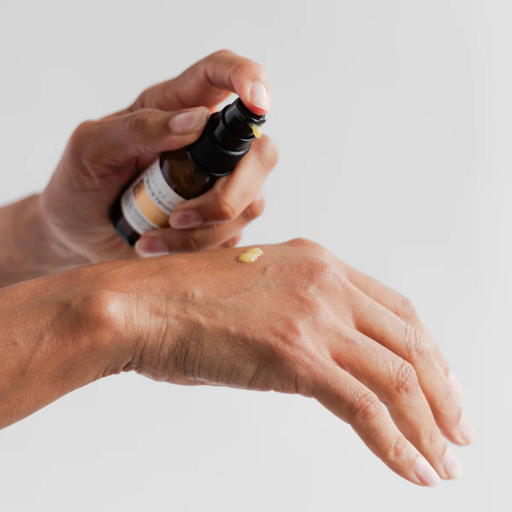 Applying skincare serum from a dropper bottle onto the back of a hand.