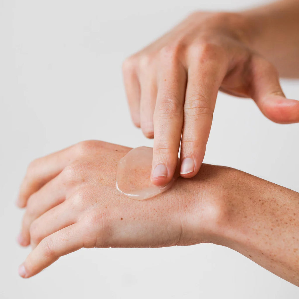 A hand is applying Marie Veronique Face To Chest Hydration Mask on the back of another hand against a plain background.