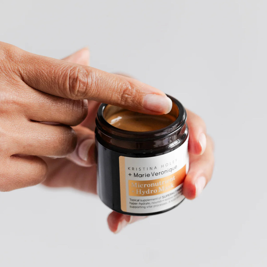 A person's fingers lifting the lid off a jar of kristina holey + marie veronique microbiome milk skincare product.