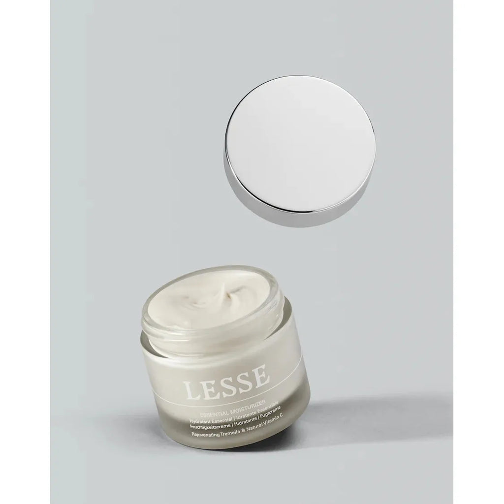 A jar of lesse moisturizing cream with its lid floating above it against a neutral background.