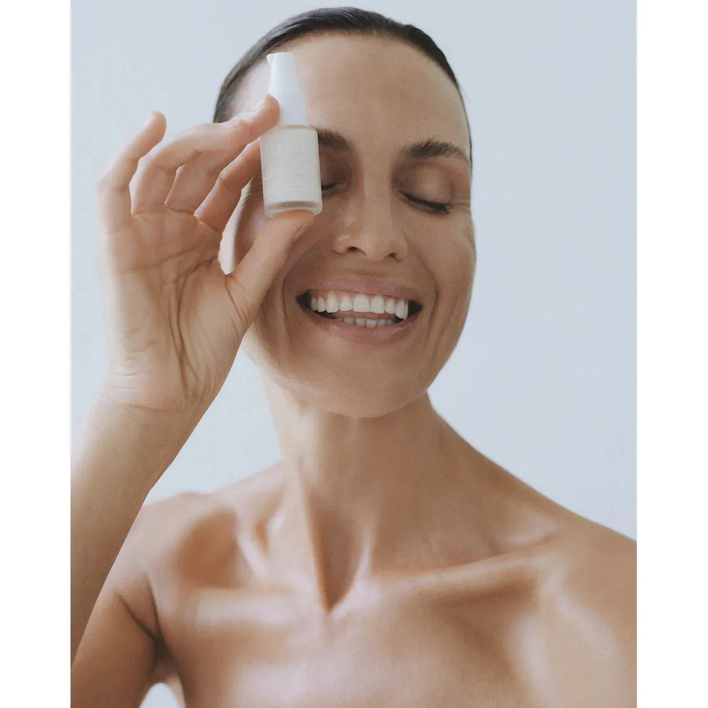 A person smiling while holding a small bottle of skincare product next to their face.