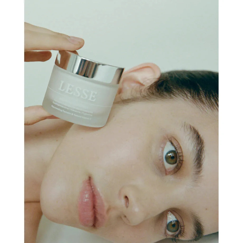 A person holding a jar of lesse skincare product near their face.