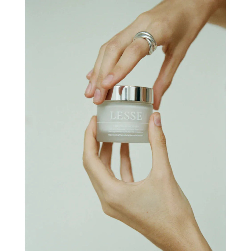 A person holding a jar of lesse skincare product with their fingertips.