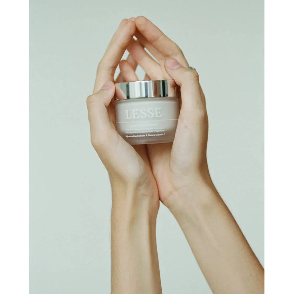 Two hands holding a jar of lesse skincare product against a neutral background.