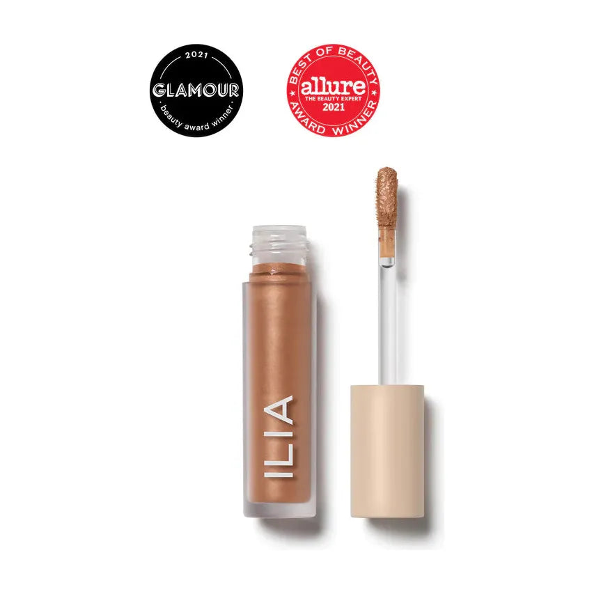 A tube of ilia brand liquid highlighter with an applicator wand, alongside award badges from glamour and allure.