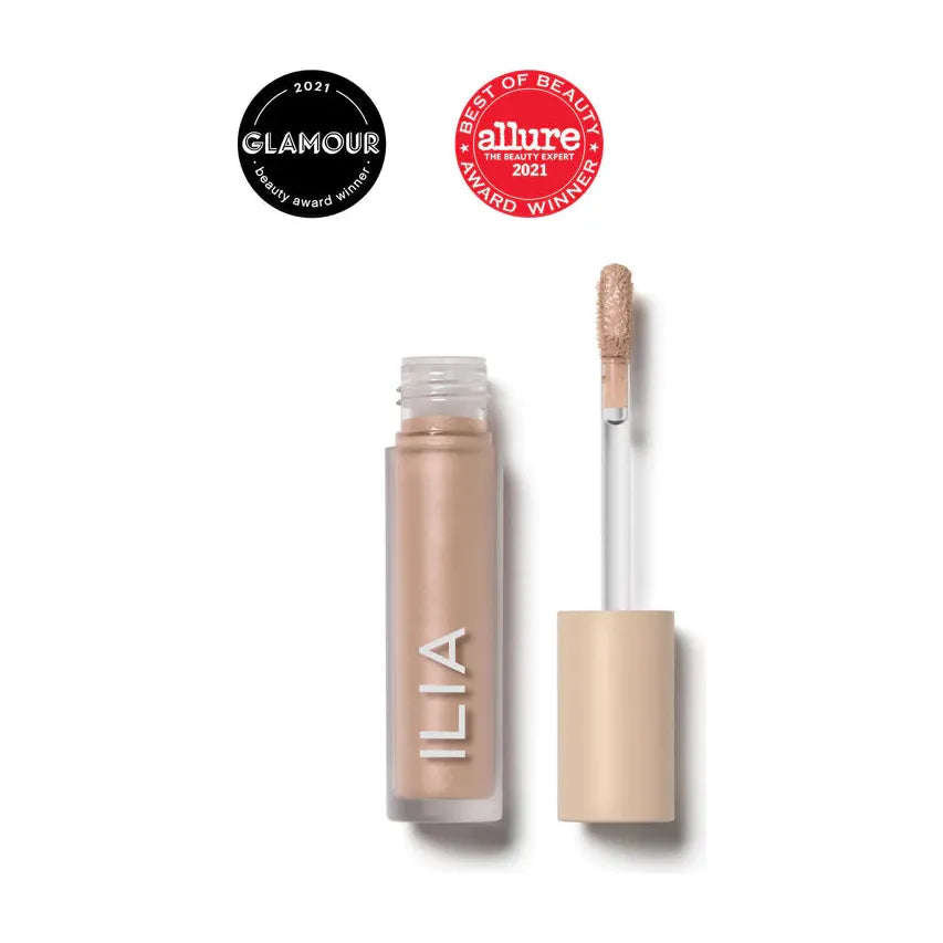 A bottle of ilia brand concealer with its applicator wand and brush tip displayed, alongside two award badges from glamour and allure for best of beauty 2021.
