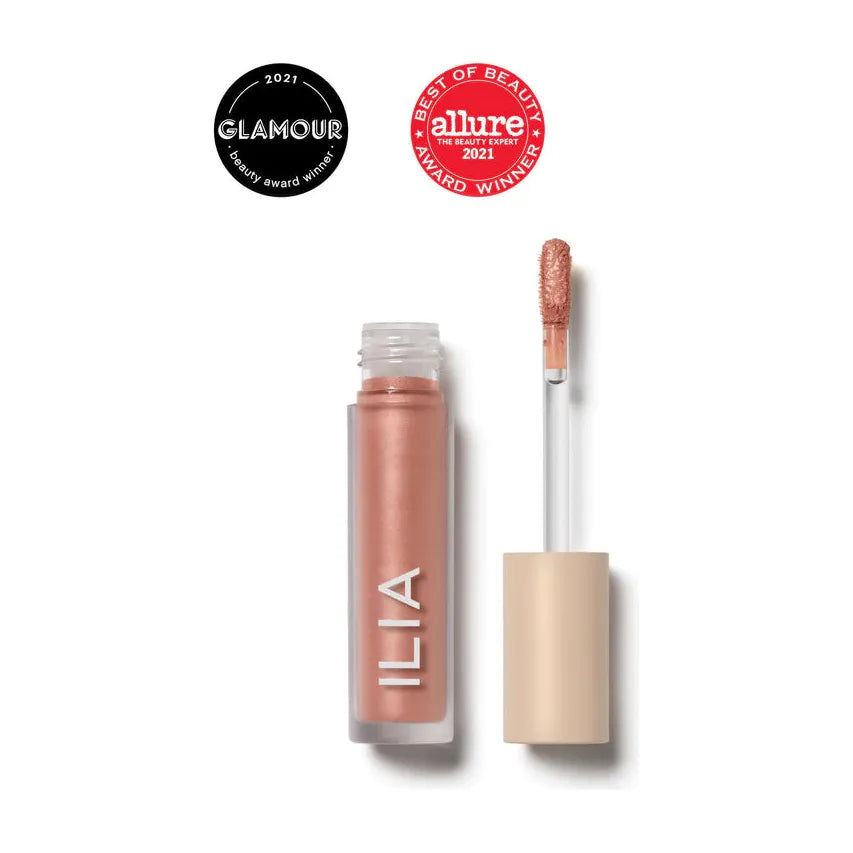 A tube of ilia lip gloss with an open cap and applicator, displaying the product color, awarded "best of beauty 2021" by allure and glamour.