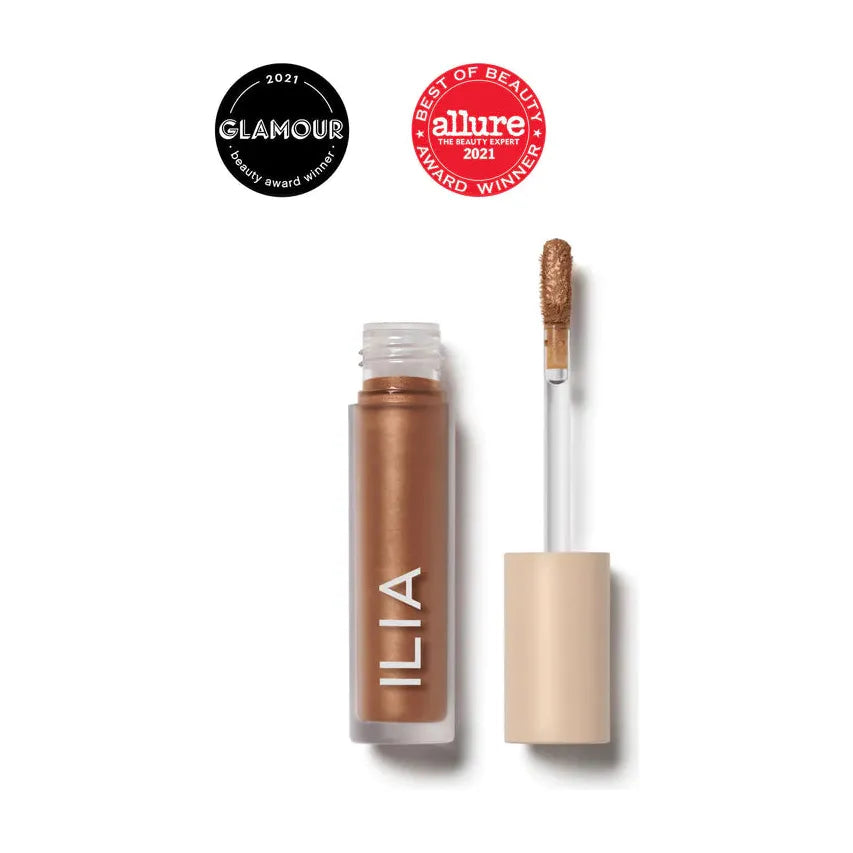 A tube of ilia brand liquid makeup product with an open cap and an applicator alongside, showing product awards from glamour and allure for 2021.