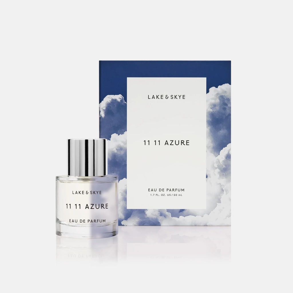 Bottle of lake & skye 11 11 azure eau de parfum in front of a blue and cloud-themed backdrop.