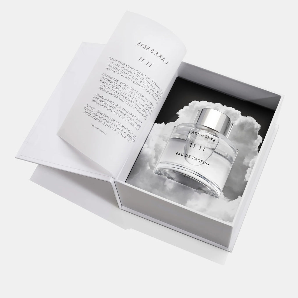 A bottle of perfume presented in an elegant box with a cloud design and an open booklet.