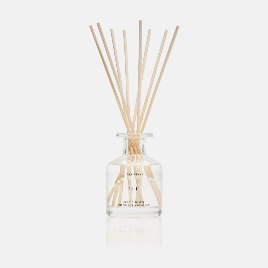 Reed diffuser with wooden sticks in a clear glass bottle against a white background.