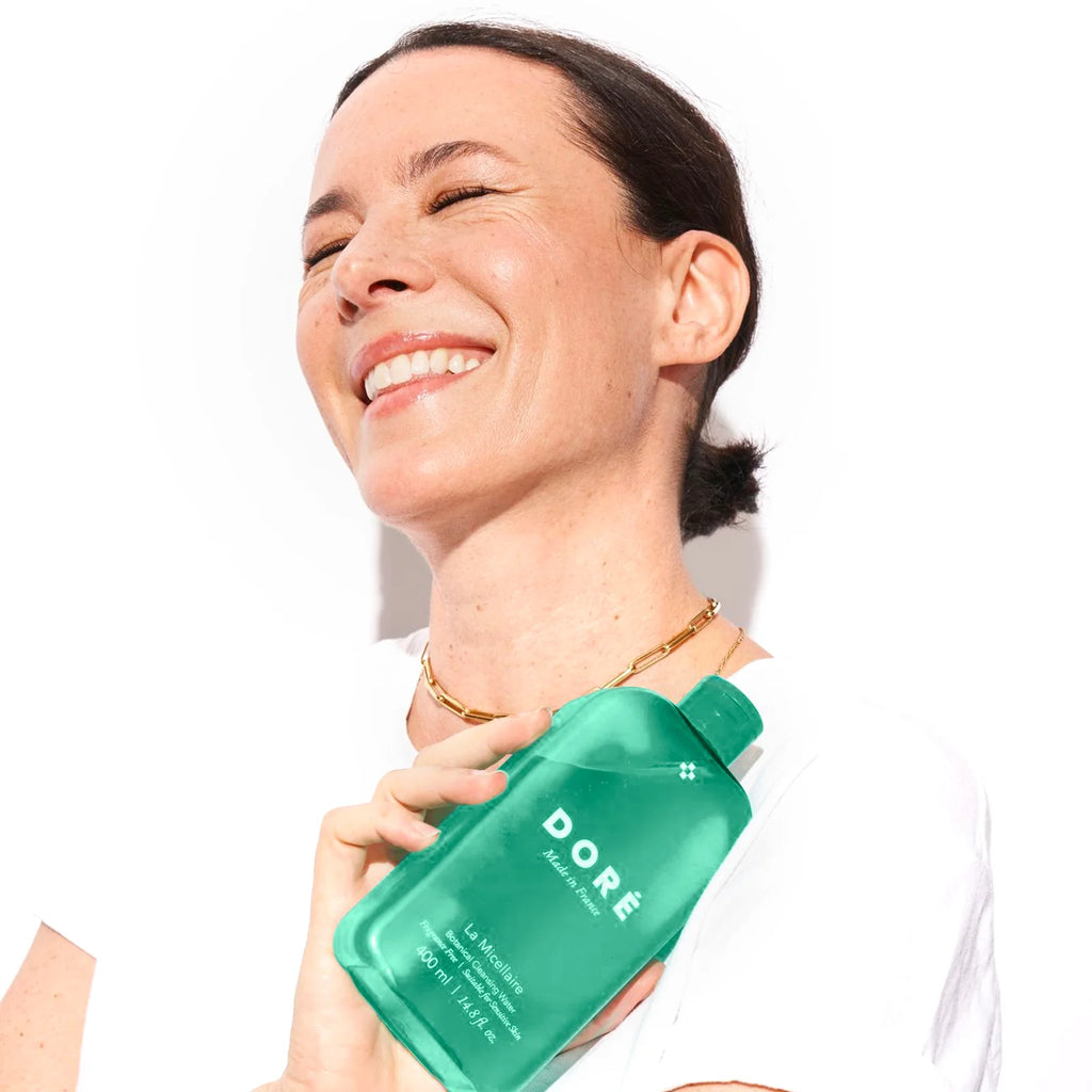 A smiling woman holding a green product bottle.