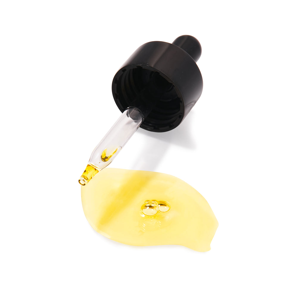 Dropper bottle dispensing a yellow liquid onto a white surface.