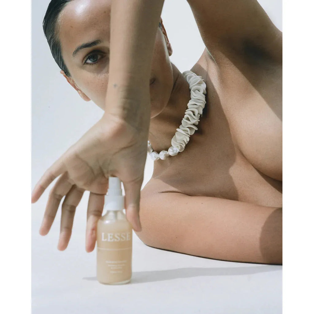 A person showcasing a lesse regeneration mist while wearing a chunky necklace.
