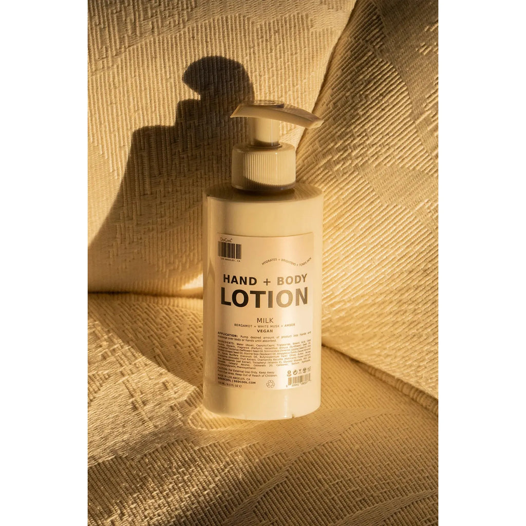 A bottle of hand and body lotion positioned in warm lighting casting a shadow on a textured background.