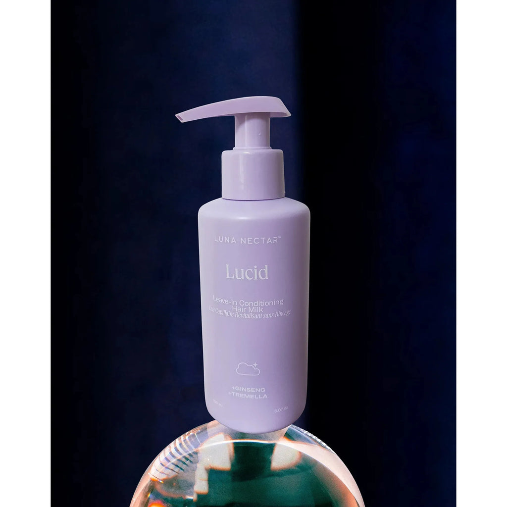 A bottle of luna nectar lucid leave-in hair conditioner is displayed against a dark background with a reflection on a glossy surface below.