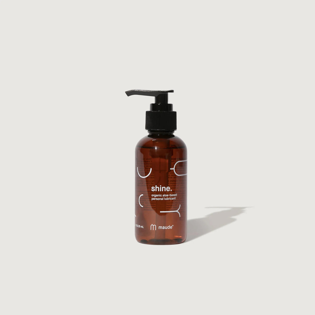 Amber glass bottle with pump containing "shine." organic personal lubricant by maude against a white background.