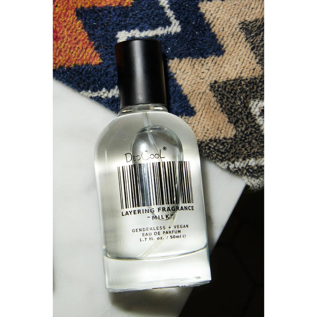 A bottle of dedcool layering fragrance on a table with a patterned textile in the background.