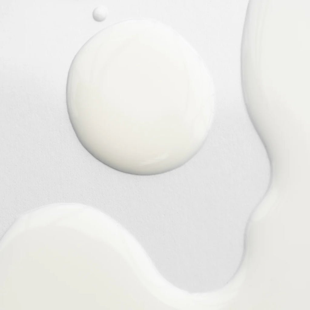 Close-up of spilled Marie Veronique Body Barrier Emulsion on a white surface, displaying a large dollop with smaller droplets around it.