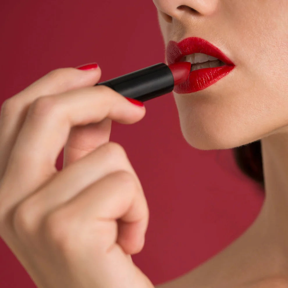A person applying red lipstick on their lips.