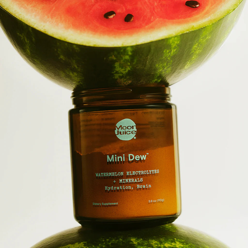 A jar of moon juice mini dew supplement placed in front of a sliced watermelon.