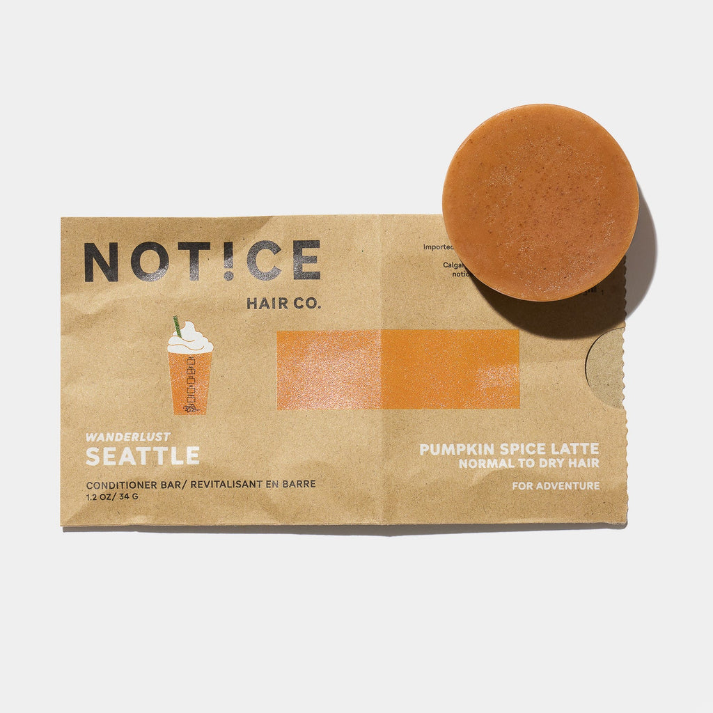 A round orange conditioner bar infused with Pumpkin Seed Oil, labeled as "NOTICE HAIR CO. SEATTLE Conditioner Bar," is designed for normal to dry hair and rests on brown packaging adorned with a charming coffee cup illustration and themed "Pumpkin Spice Latte.