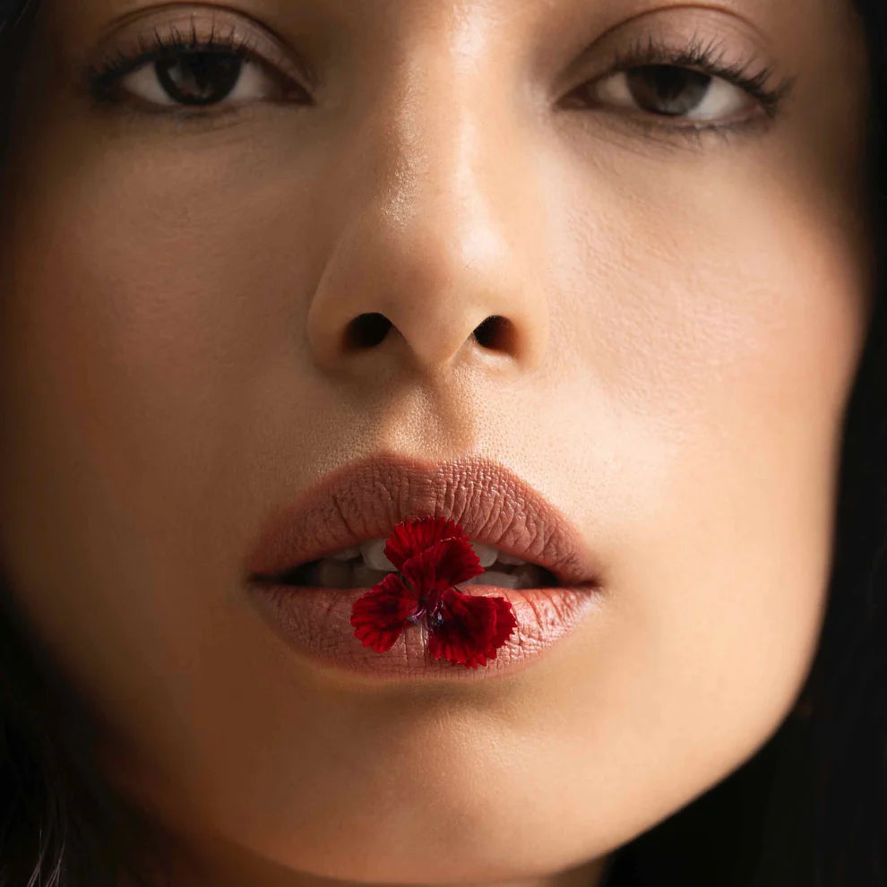 Close-up of a woman with a red flower petal between her lips.
