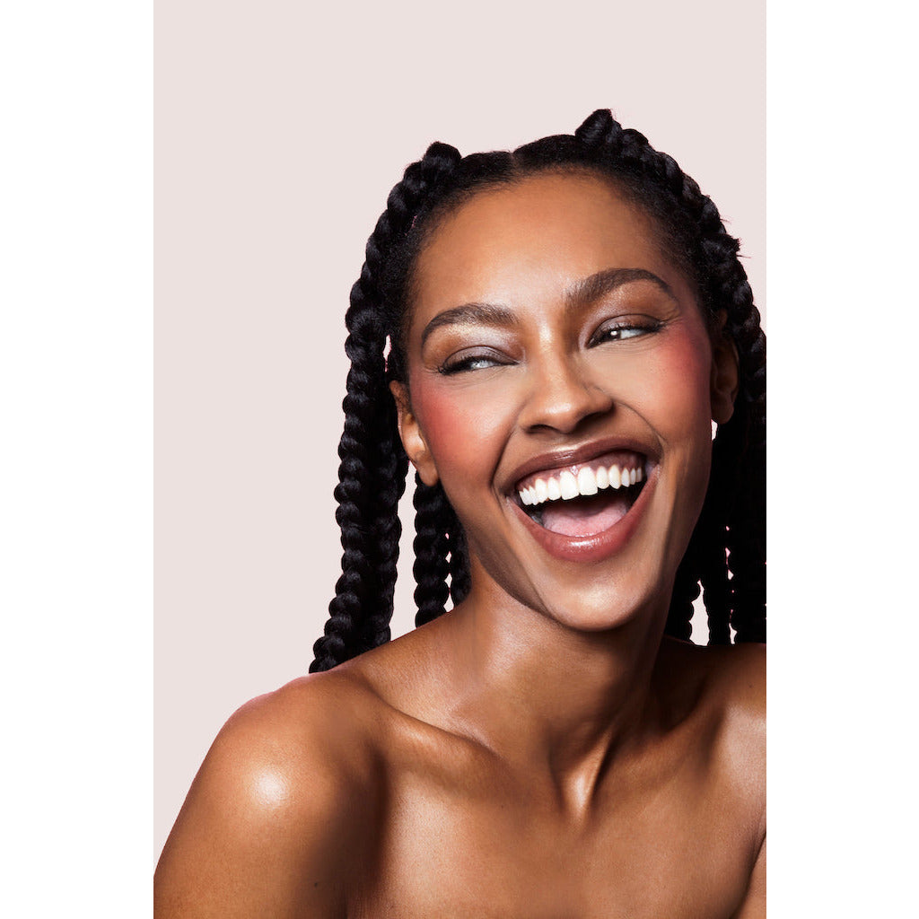 A woman with braided hair laughing against a neutral background.