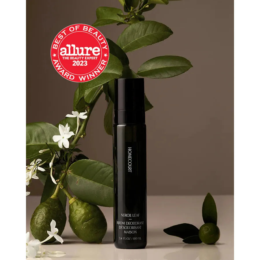 A cosmetic spray bottle labeled "Homecourt Room Deodorant" displayed with a branch of green leaves and white flowers, marked with a red "allure best of beauty 2023 award winner" badge.