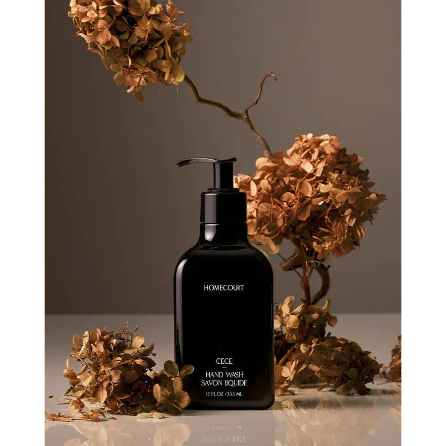 Black bottle of liquid hand wash with a label, accompanied by dried hydrangea flowers, against a neutral background.