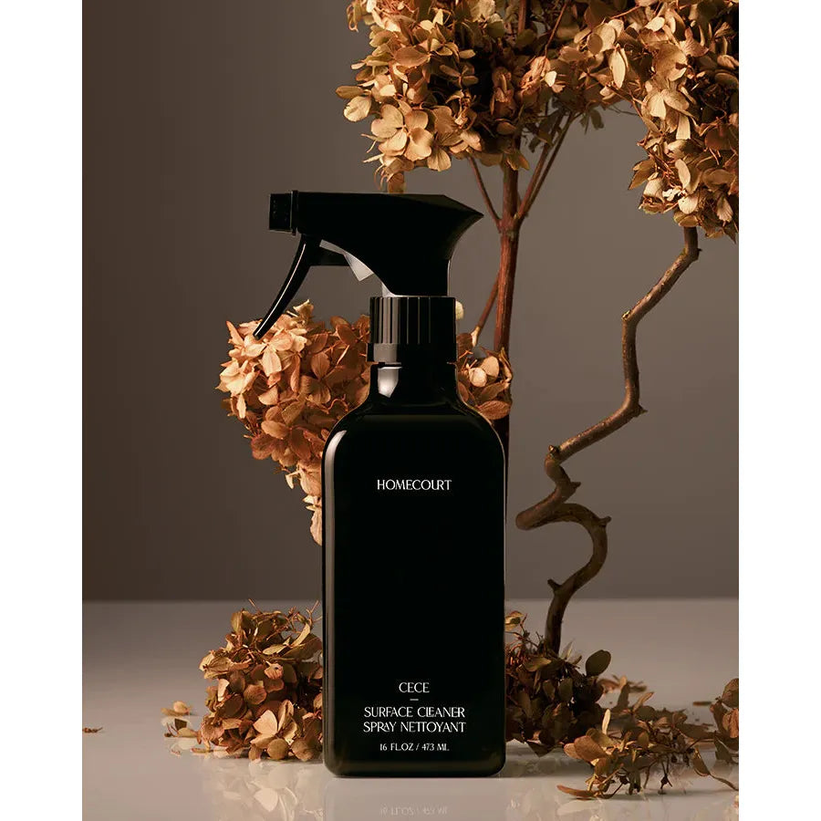 A bottle of homecourt surface cleaner spray alongside dried flowers against a neutral background.