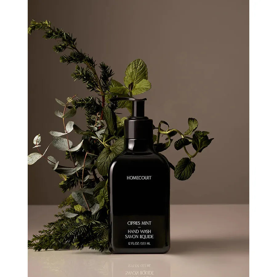 A bottle of homecourt cypress mint hand wash amidst a backdrop of green foliage.