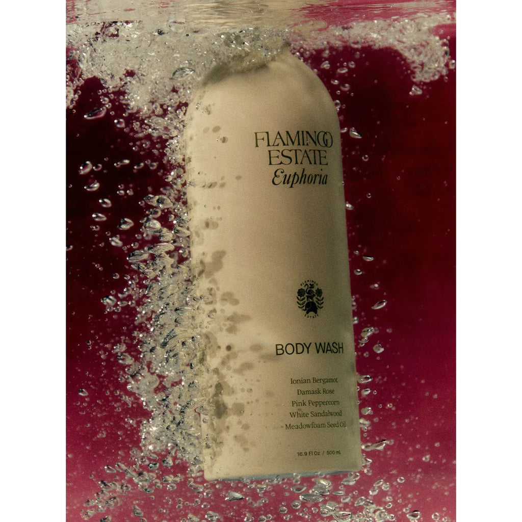 A bottle of flamingo estate euphoria body wash immersed in water with bubbles surrounding it.