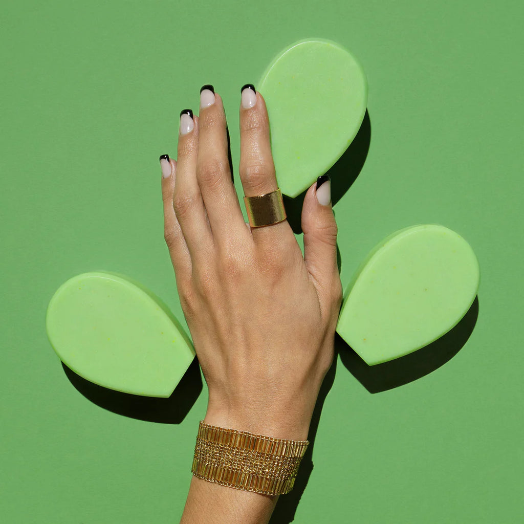 A hand with black and white nail polish against a green background, positioned between two green, leaf-shaped objects.