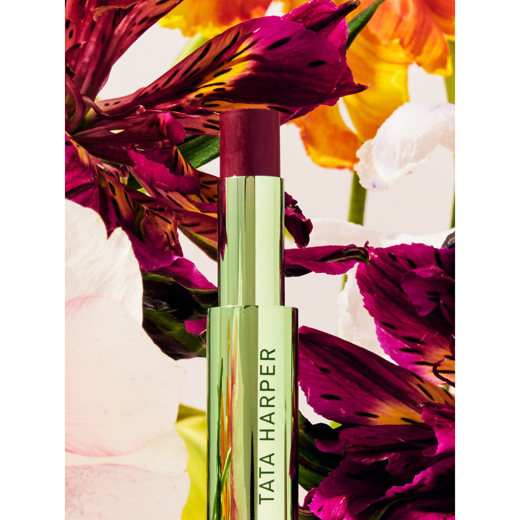 A lip treatment product by tata harper displayed among vibrant flowers.