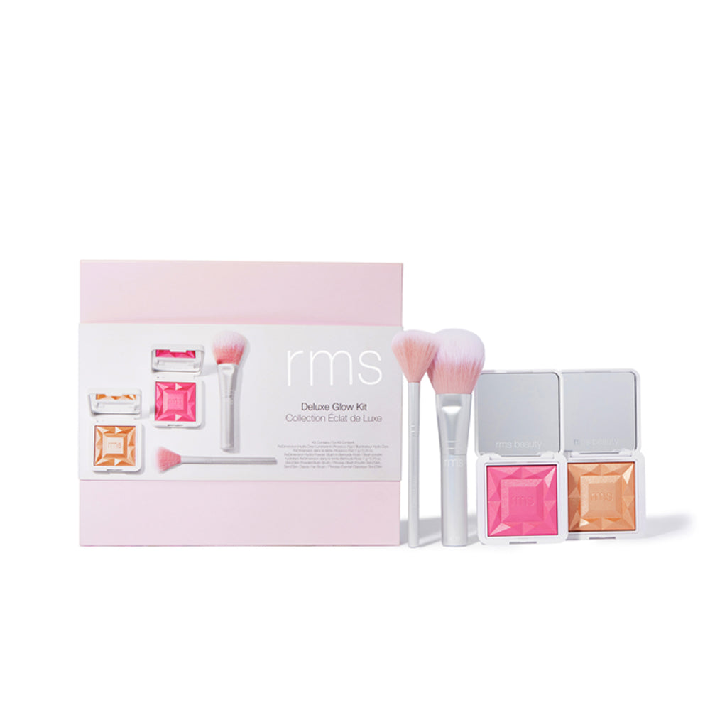 A makeup set by rms beauty featuring brushes, compact powders, and lip balm against a pale pink background.