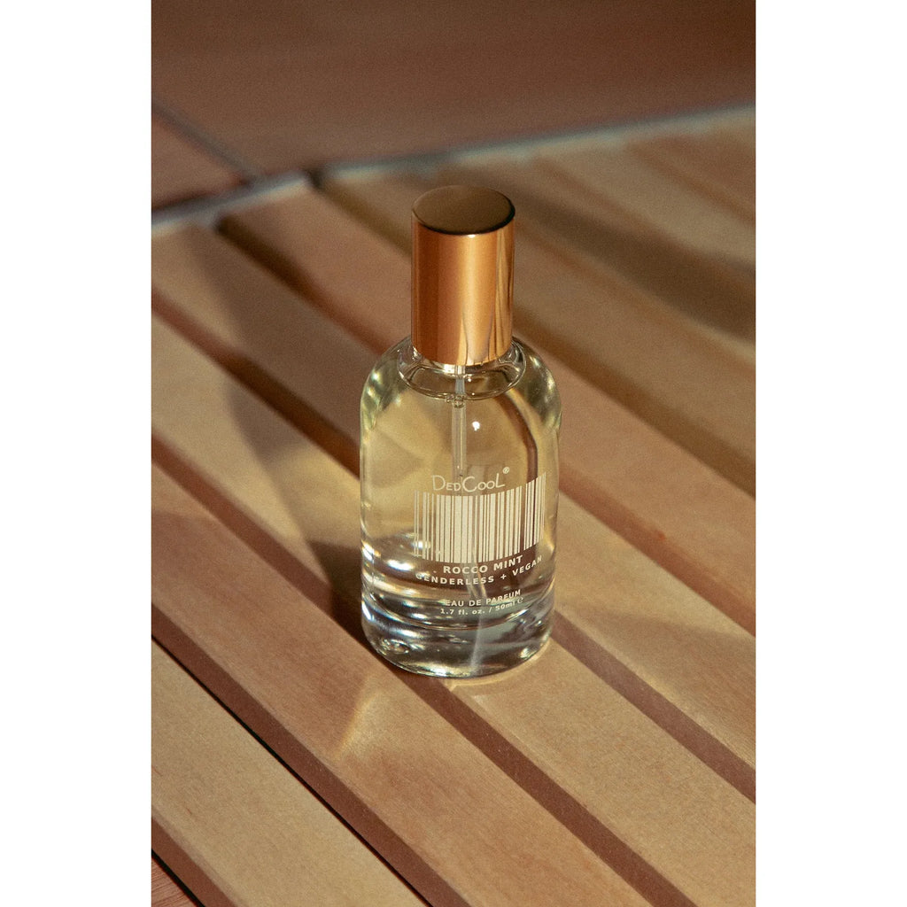 A bottle of perfume on a wooden slatted surface with sunlight casting shadows.
