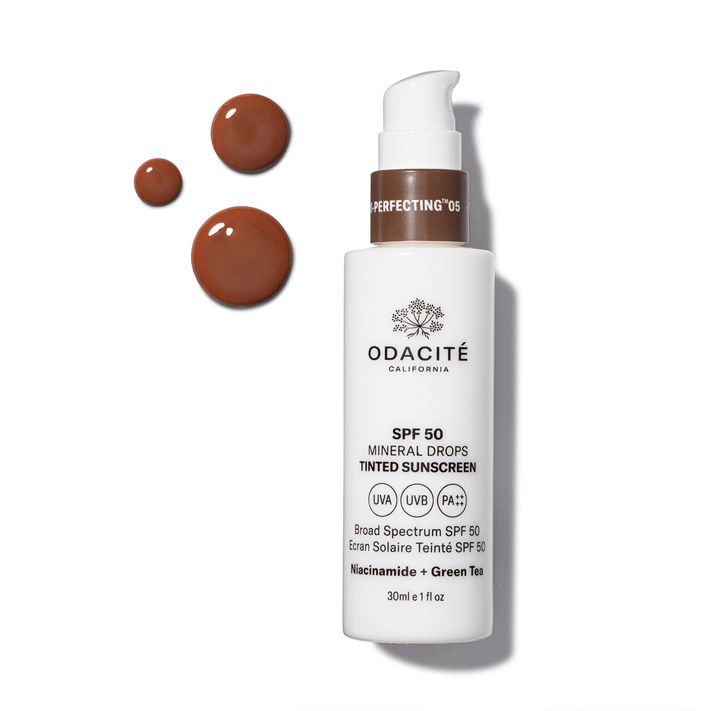 A bottle of odacite tinted mineral sunscreen with spf 50 alongside three droplets of the product.