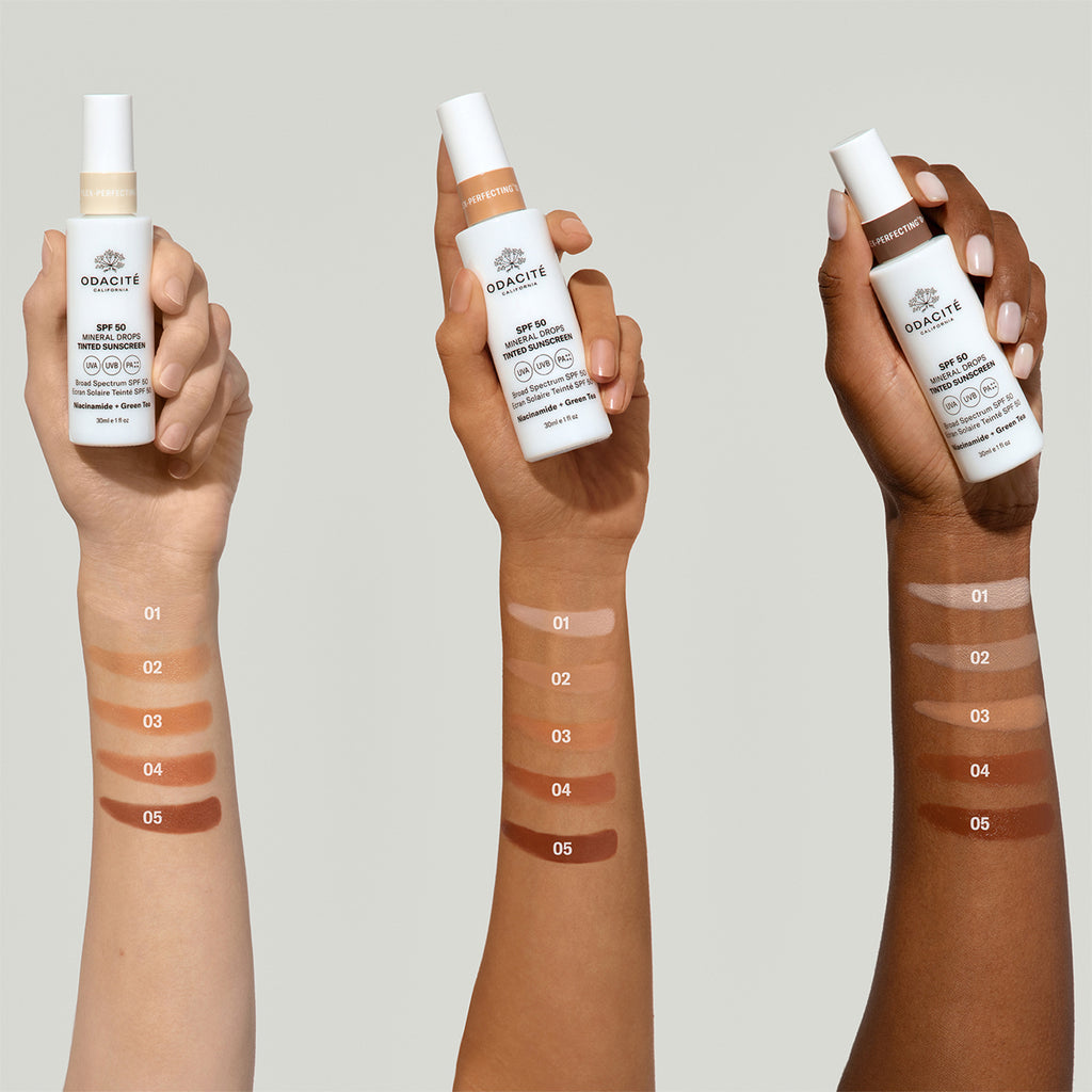 Three hands of varying skin tones displaying swatches of foundation shades on their forearms with the corresponding foundation bottles held above.