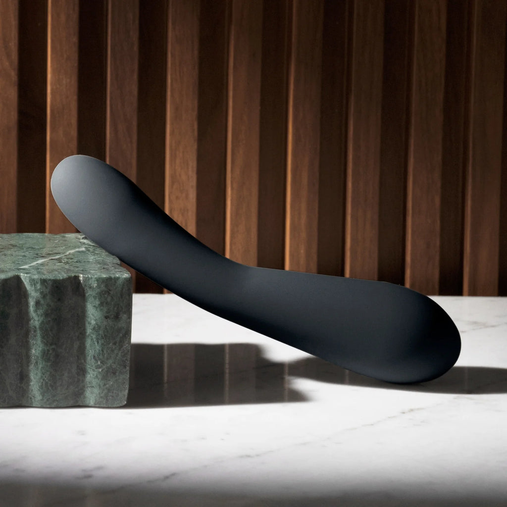 A black sculptural object on a marble surface against a wooden backdrop.