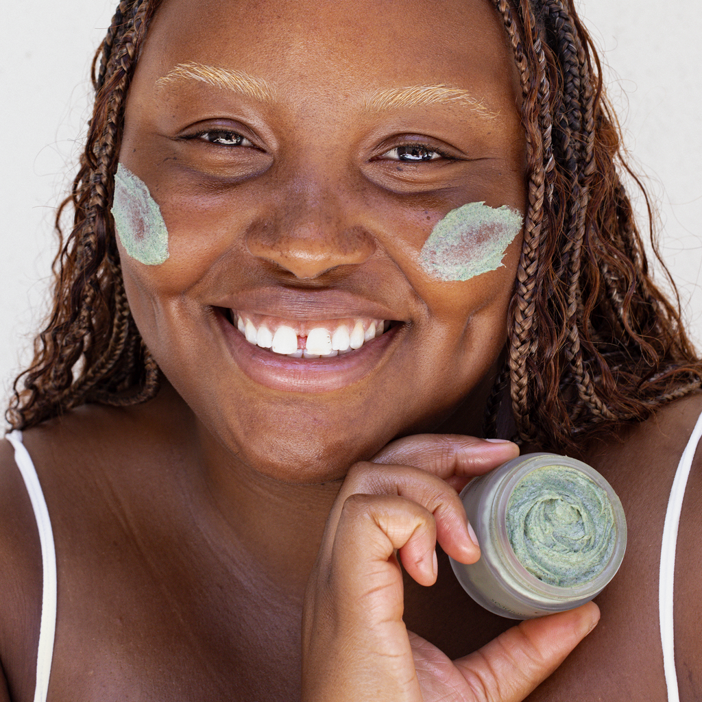 A woman smiling while holding a green face mask.