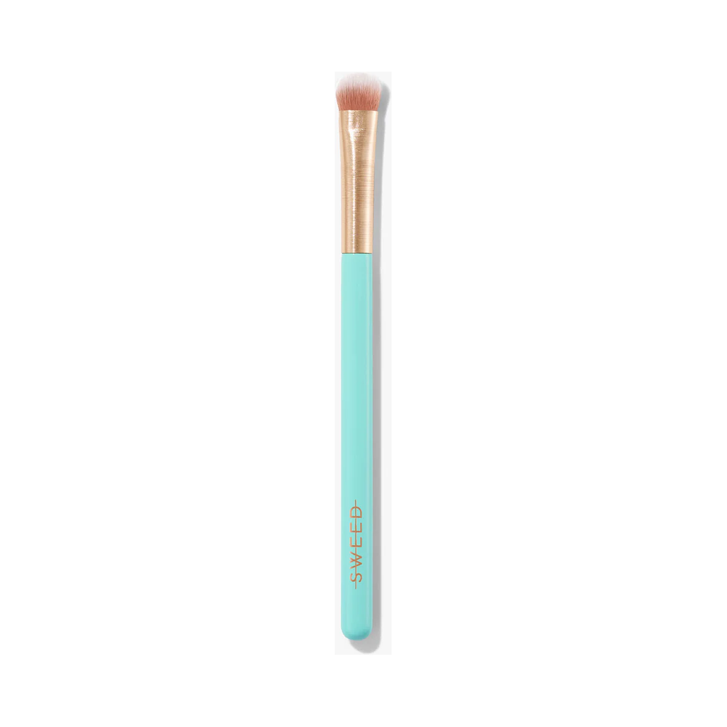 The Sweed 06 Eyeshadow Brush features a light blue handle and metallic gold ferrule, with short, dense bristles and a synthetic flat rounded tip that is perfect for controlled eyeshadow application.