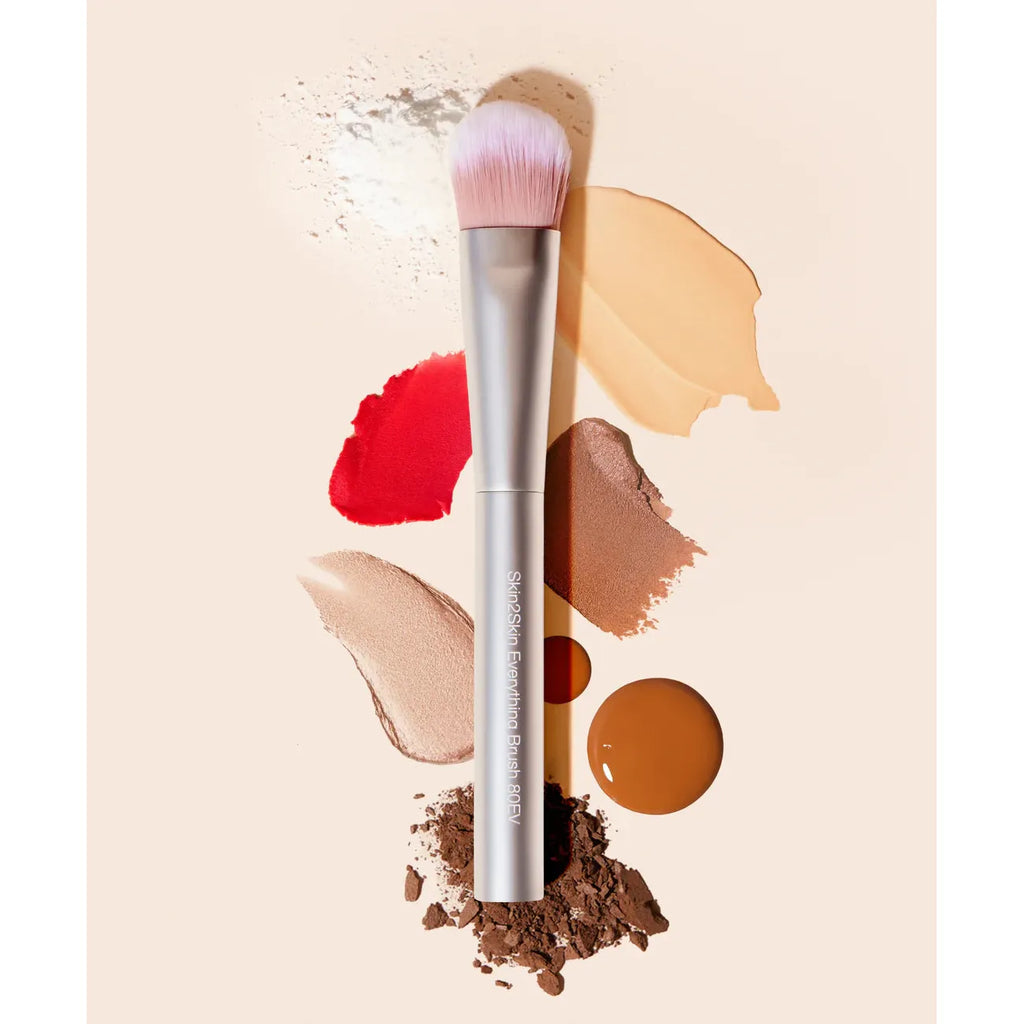 Makeup brush surrounded by various cosmetic products and powder smears.