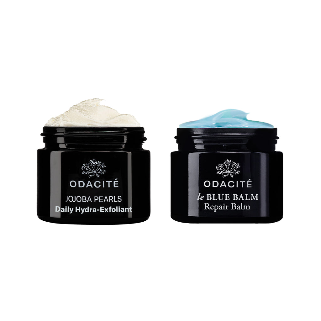 Two jars of odacite skincare products, one labeled "daily hydra-exfoliant" with a cream on top, and the other labeled "le blue balm" with a blue cream on.