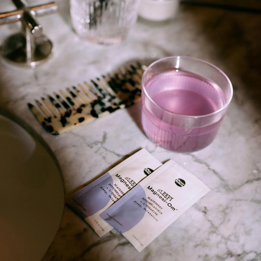 A glass of pink liquid next to two sachets of medicine on a bathroom counter.