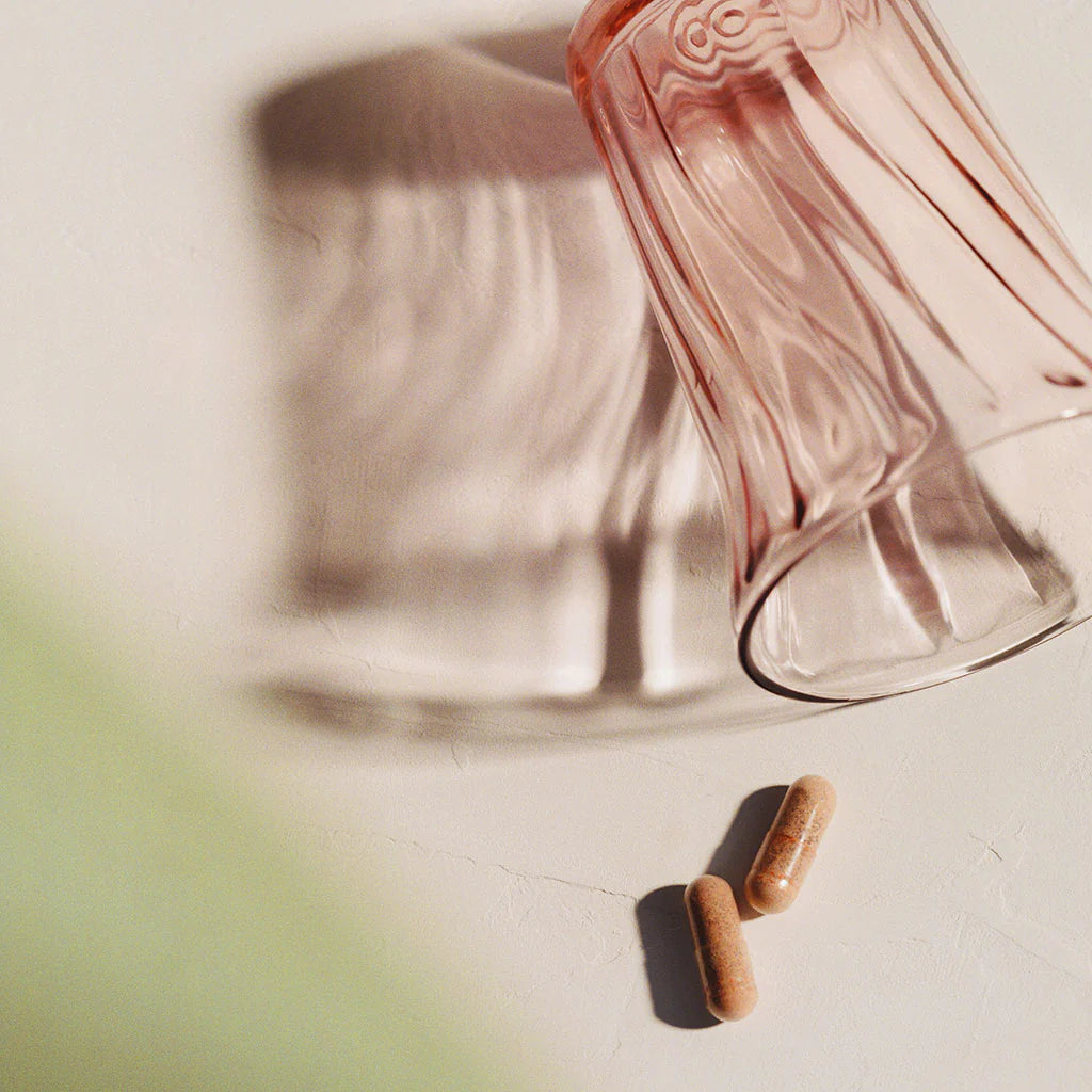 Top-down view of two capsules next to an overturned glass bottle casting a shadow on a table.