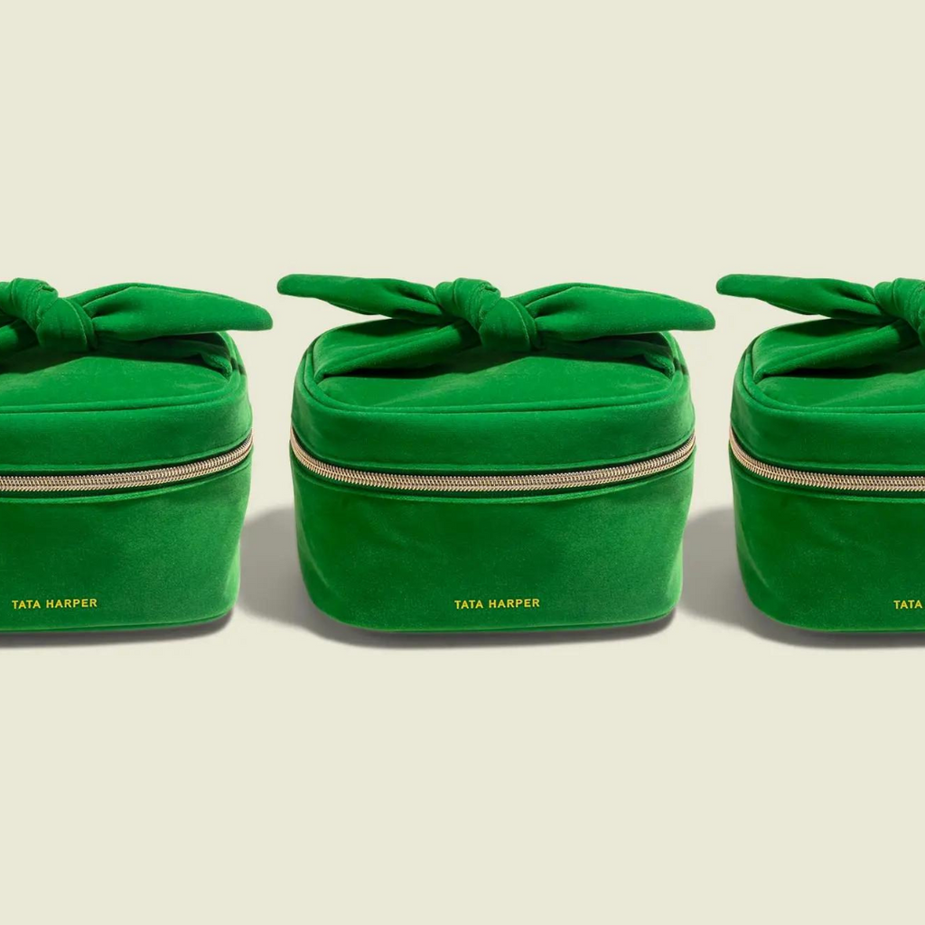 Three green velvet cosmetic bags with gold zippers and knotted ties, labeled "Wren and Wild x Tata Harper Glow Getter 30 Minute Flash Facial Event," aligned in a row against a light background.